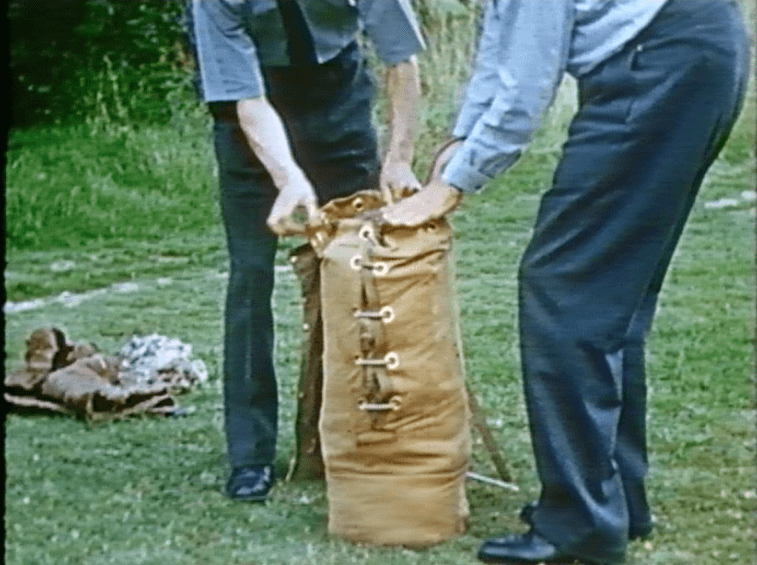 Two men demonstrating a paratroop kit bag and beacon